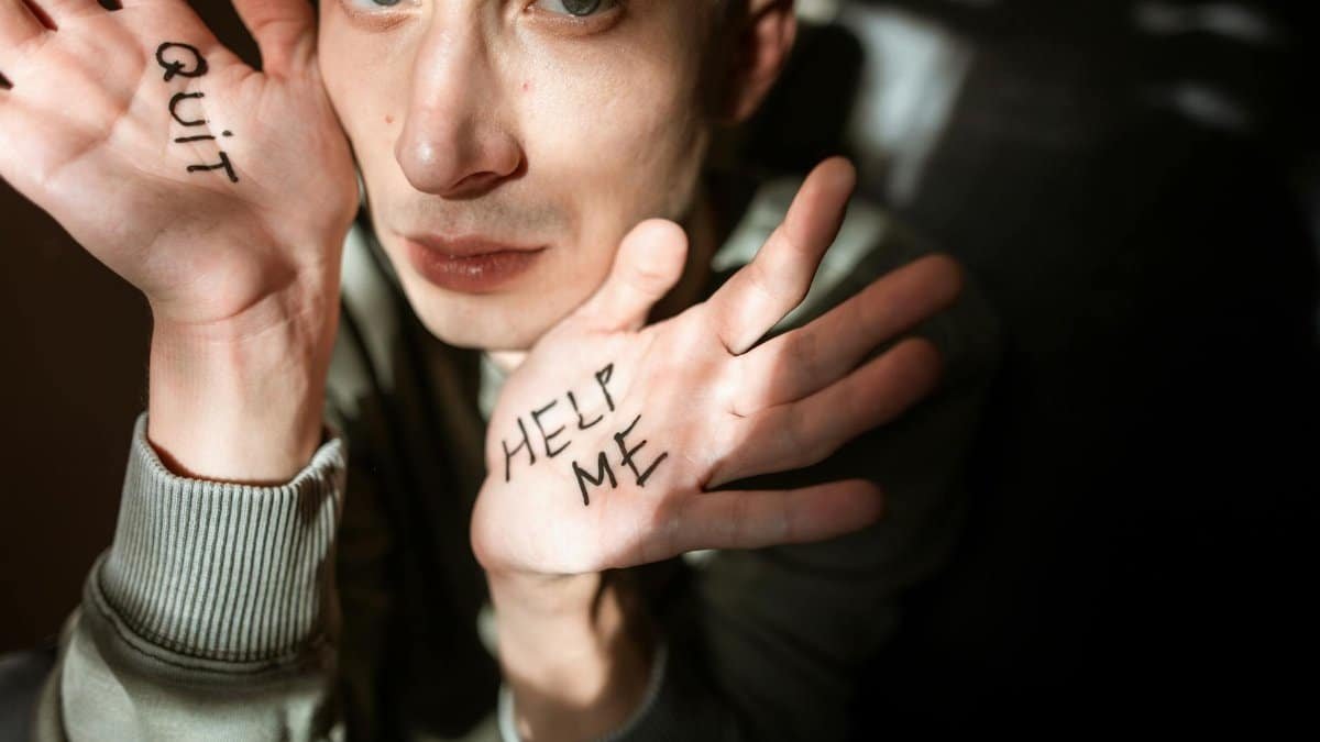 Close-up of a person showing palms with 'Help Me' and 'Quit' written, expressing emotions.