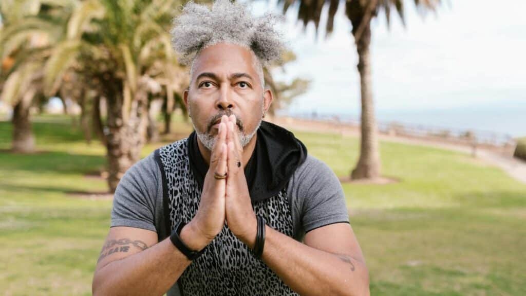 Man in a meditative yoga pose amid palm trees, embodying concentration and wellness outdoors.