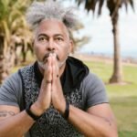 Man in a meditative yoga pose amid palm trees, embodying concentration and wellness outdoors.