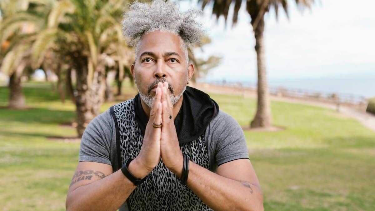 Man in a meditative yoga pose amid palm trees, embodying concentration and wellness outdoors.