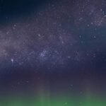 Marvel at the breathtaking view of the aurora borealis under the Milky Way in a starry night sky.