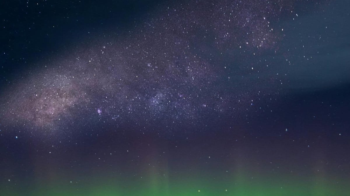 Marvel at the breathtaking view of the aurora borealis under the Milky Way in a starry night sky.