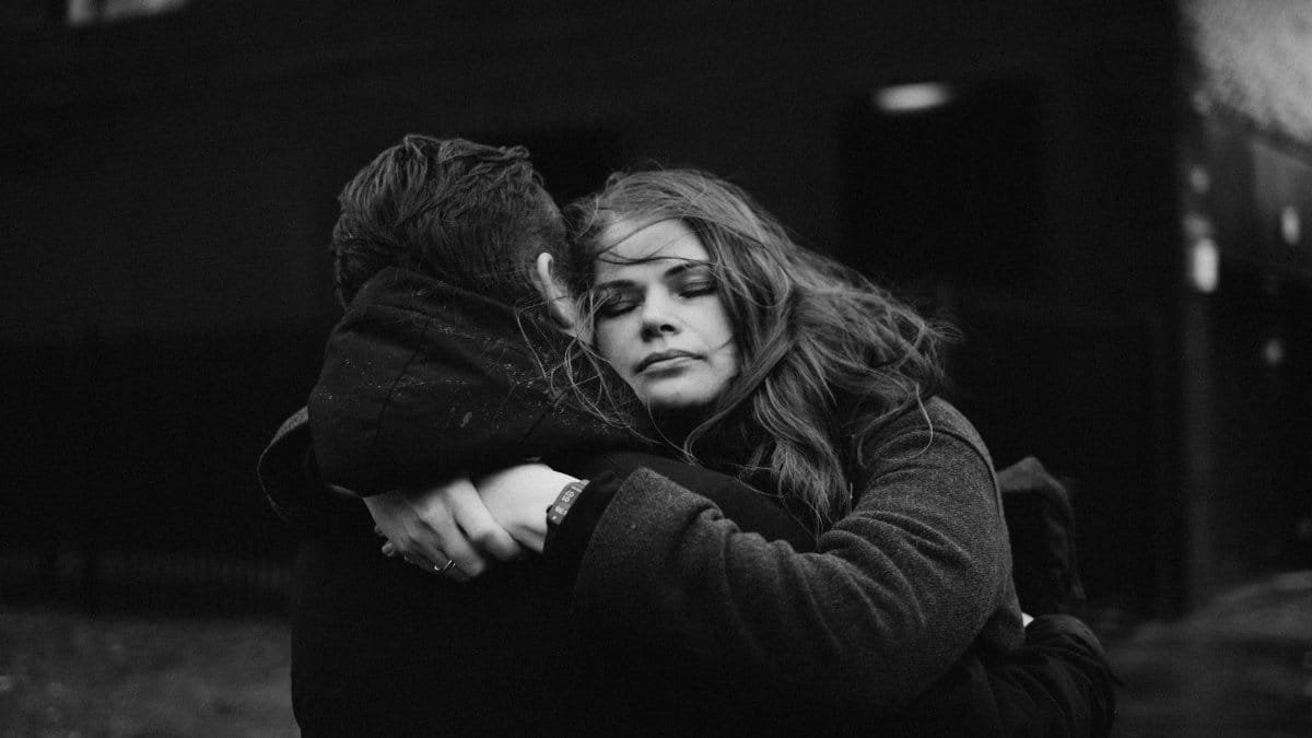 A dramatic black and white photograph capturing a couple embracing outdoors, eyes closed, conveying emotion and connection.