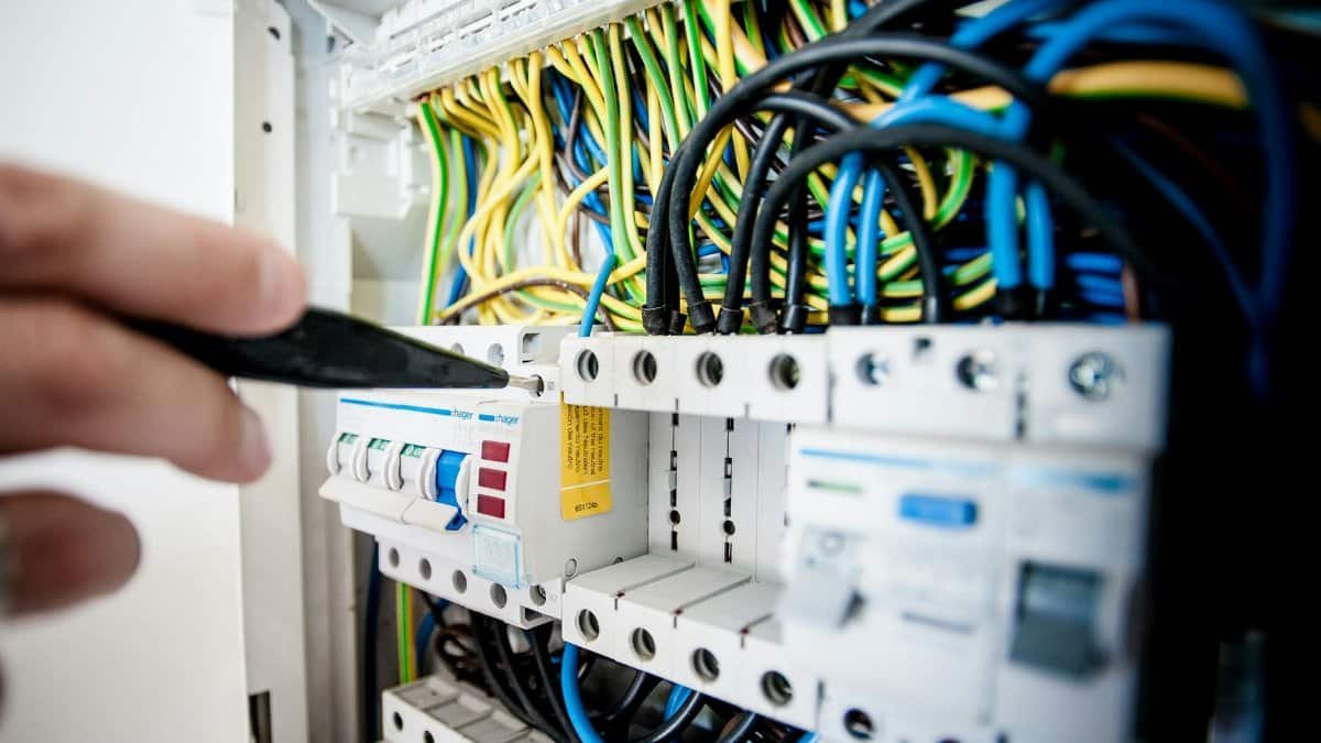 Hand of electrician working on a circuit breaker panel with colorful wires, ensuring safe electrical connections.