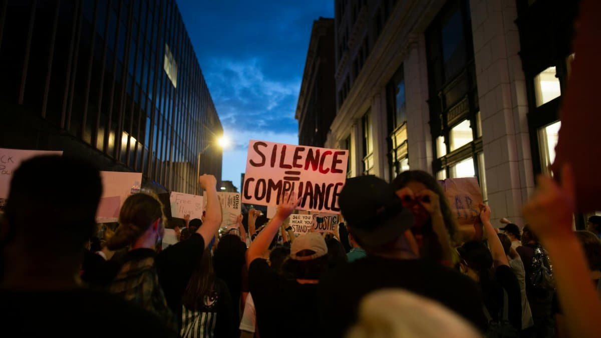 Back view crowd of faceless people walking on street with banners between modern buildings during demonstration in evening