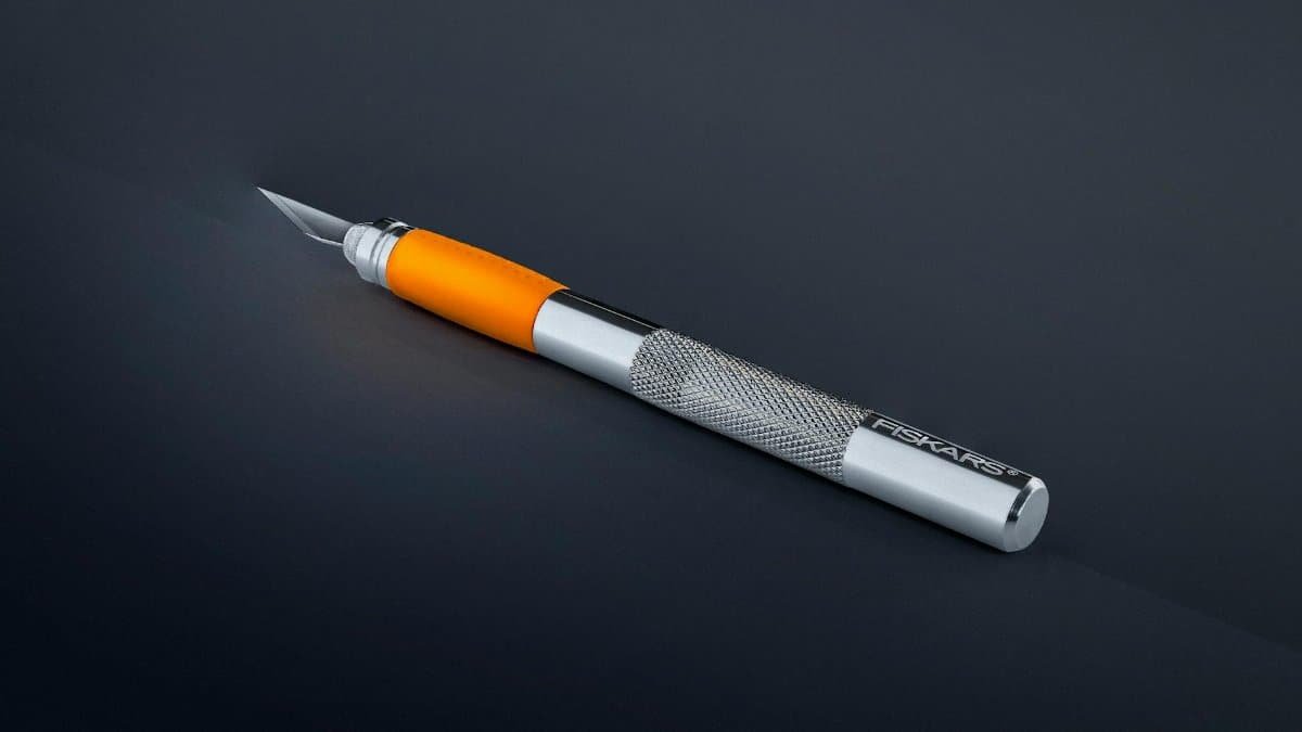 Sharp craft knife with orange and silver handle on a dark studio background.