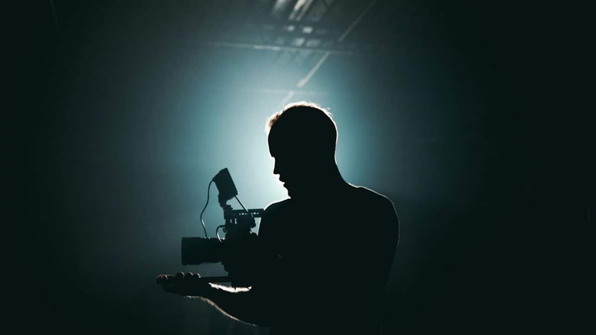 Silhouette of a cinematographer with camera gear in a dramatic, low light setting.