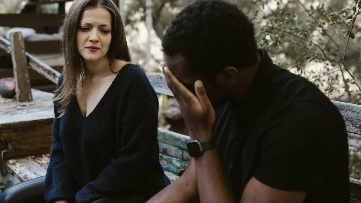 A couple experiencing emotional tension during a conversation outside on a bench.