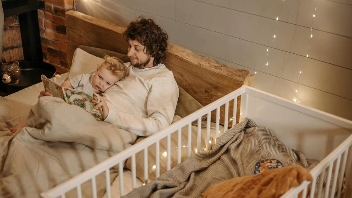 A father and child enjoy a bedtime story together in a warmly lit bedroom.