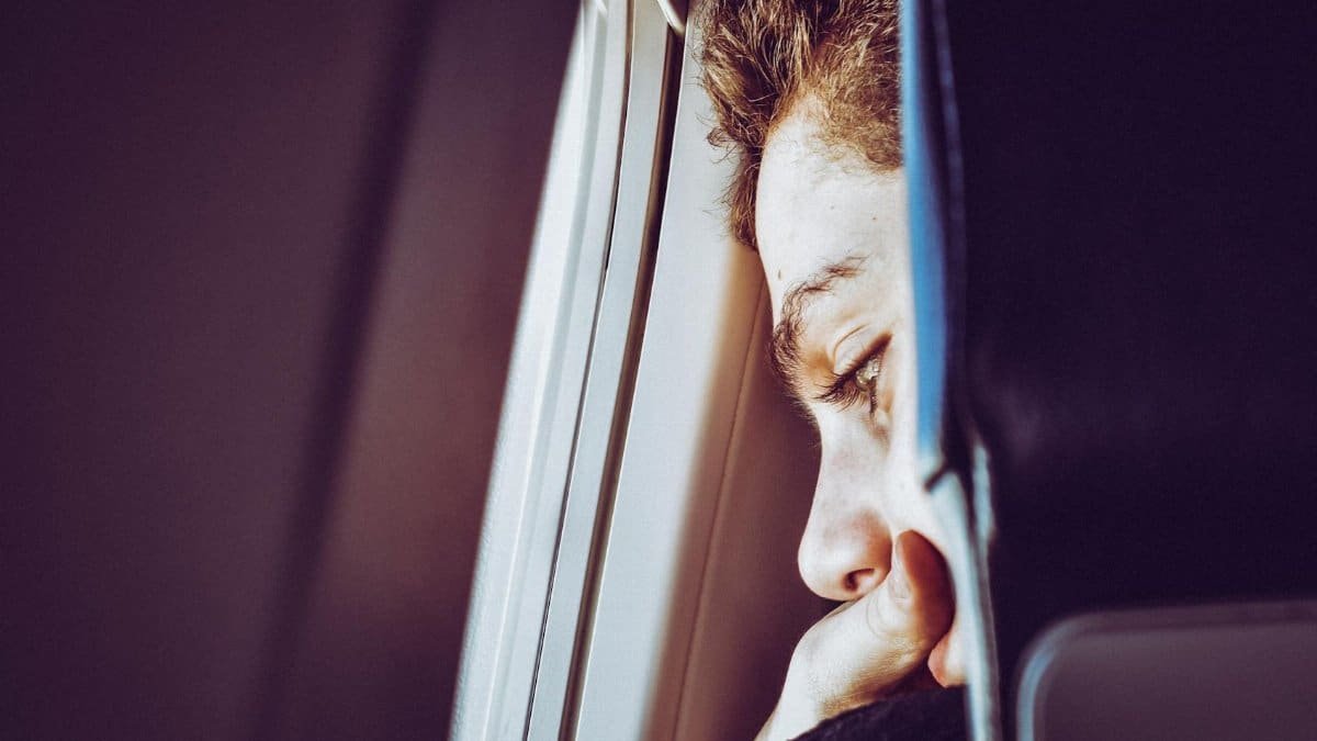 A young man looks thoughtfully out of an airplane window, captured in a close-up portrait.
