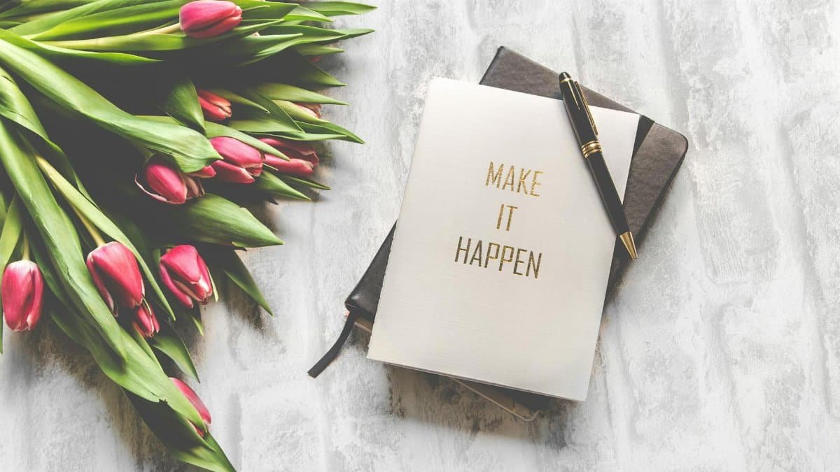 A notebook with 'Make It Happen' inscription beside a bouquet of pink tulips, capturing inspiration.