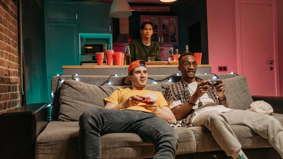 Three friends having a relaxed evening playing video games at home with drinks.