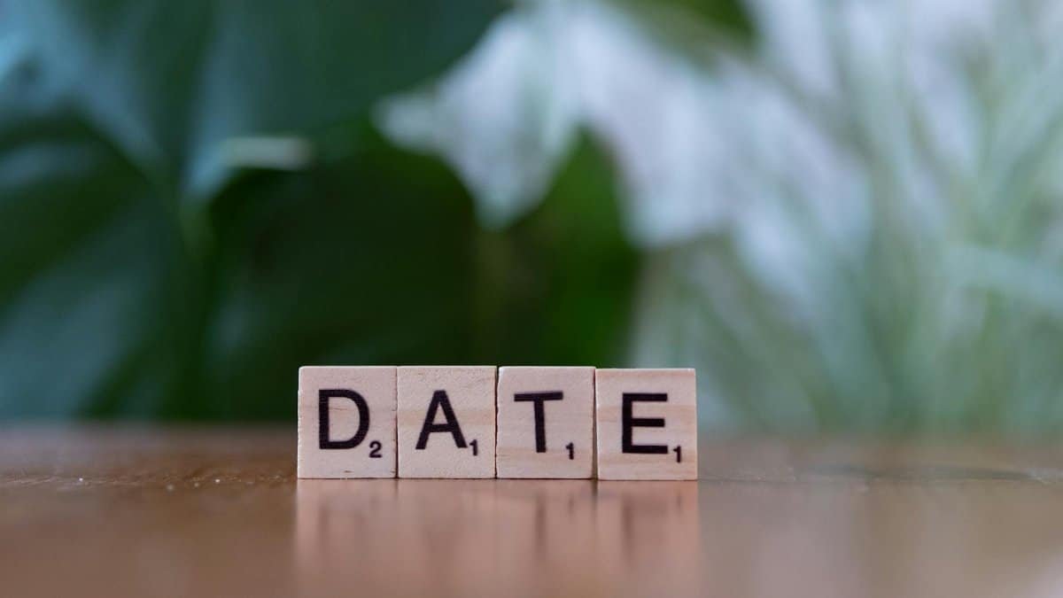 Wooden Scrabble tiles forming the word 'DATE' against a green blurred background.