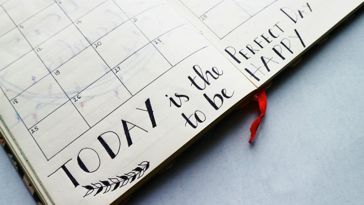 Open planner with handwritten quotes and calendar layout, promoting positivity and organization.