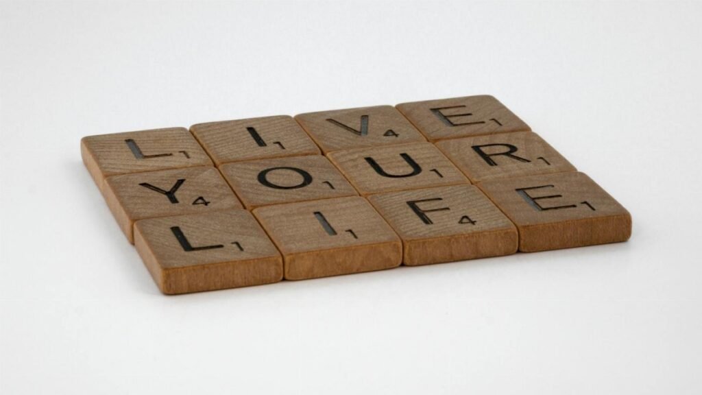 Wooden Scrabble tiles spell out 'Live Your Life' on a white surface. Encouraging and minimalist.