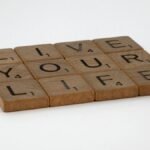 Wooden Scrabble tiles spell out 'Live Your Life' on a white surface. Encouraging and minimalist.