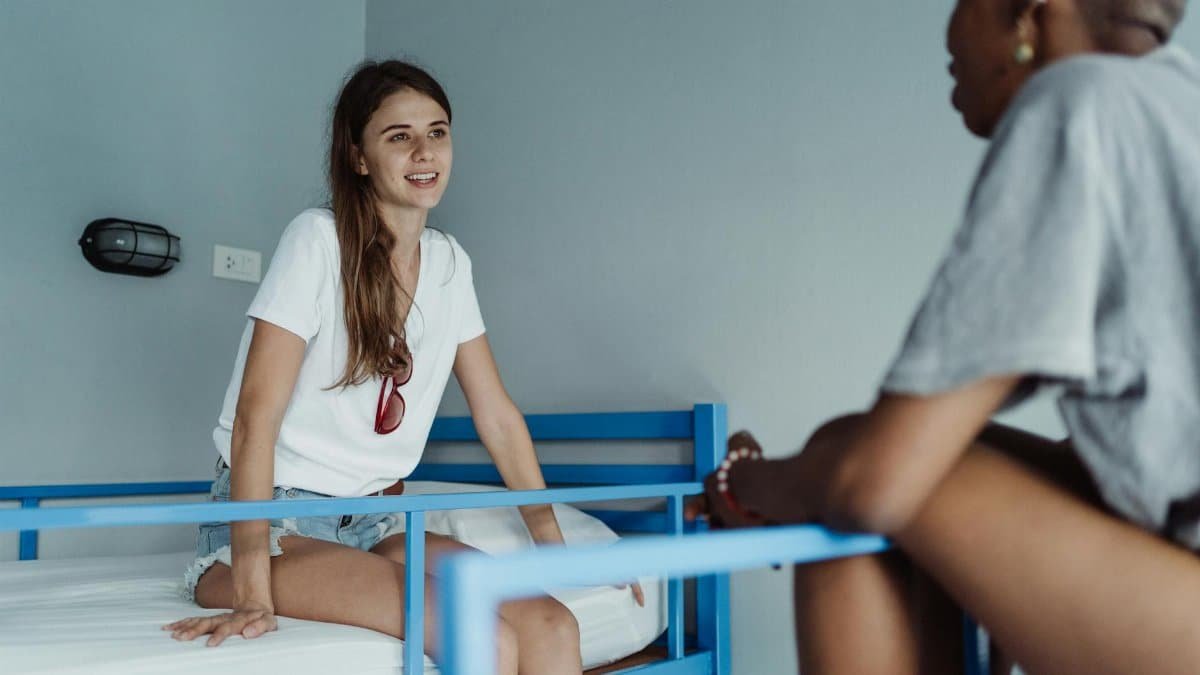 Two women engaged in a friendly conversation in a hostel room with bunk beds.