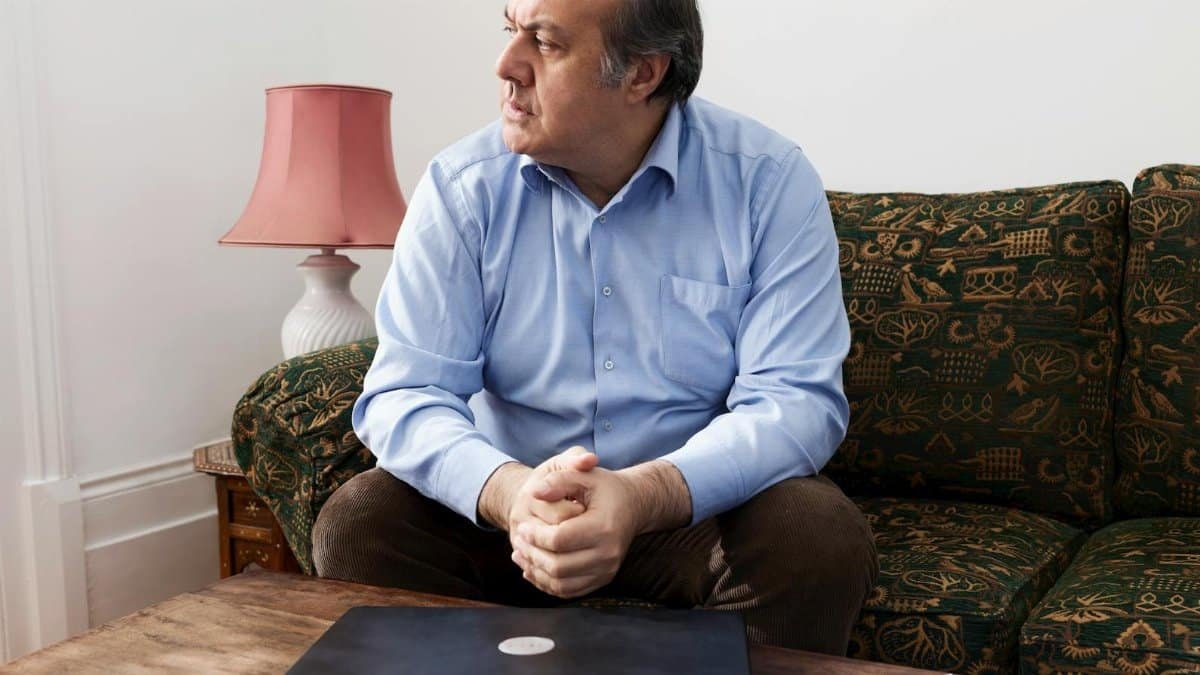 Middle-aged man sitting on a couch beside a closed laptop, depicting digital disconnection.