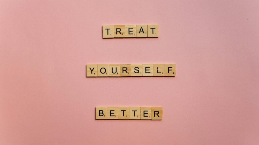 Wooden tiles on a pink background spelling 'Treat Yourself Better'. Ideal for self-care and motivation themes.