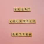 Wooden tiles on a pink background spelling 'Treat Yourself Better'. Ideal for self-care and motivation themes.