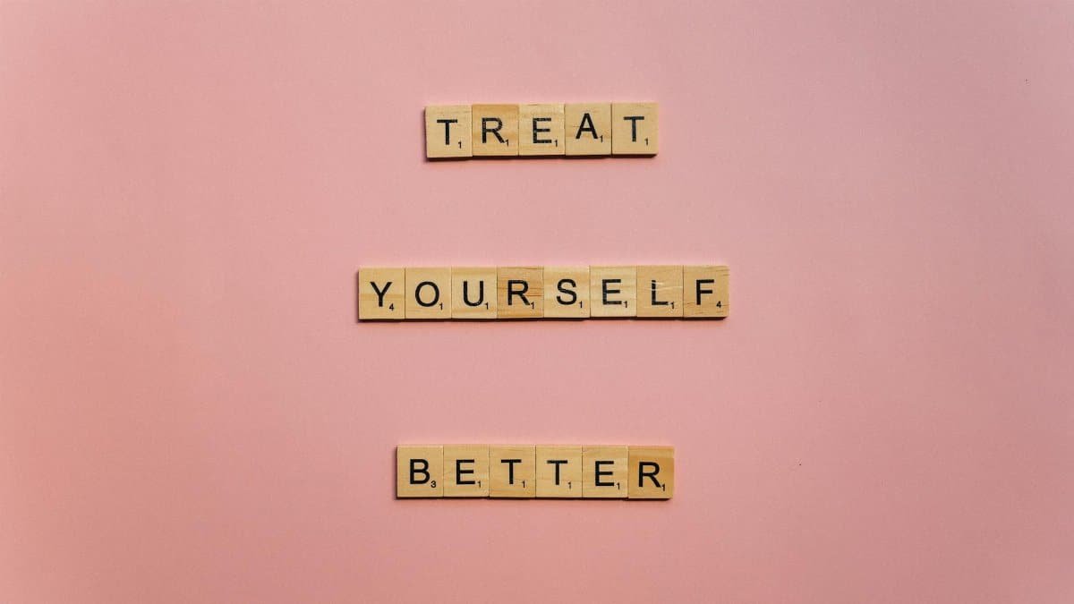 Wooden tiles on a pink background spelling 'Treat Yourself Better'. Ideal for self-care and motivation themes.
