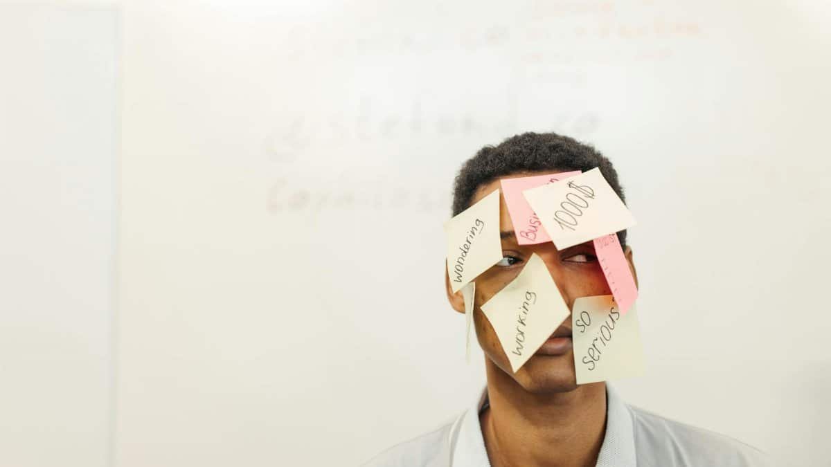 Young man with sticky notes on his face representing creative office thinking and multitasking.