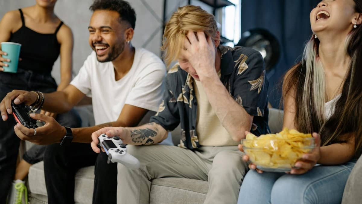 Diverse group of friends having fun playing video games indoors, sharing laughter and snacks.
