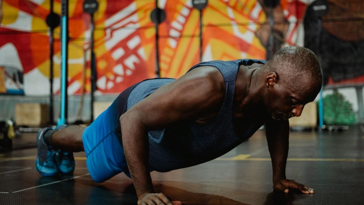 Adult man doing push-ups in a colorful gym setting, promoting fitness and health.