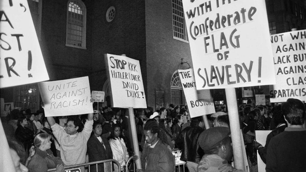 Black and white image of a diverse crowd protesting against racism, holding impactful signs.