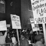 Black and white image of a diverse crowd protesting against racism, holding impactful signs.