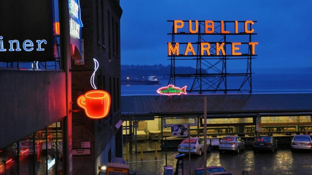 Vibrant nighttime view of Seattle's Public Market with neon coffee and market signs illuminated.