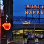 Vibrant nighttime view of Seattle's Public Market with neon coffee and market signs illuminated.