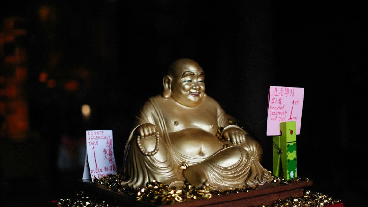 Gold Laughing Buddha statue adorned with donation signs and coins, symbolizing prosperity.