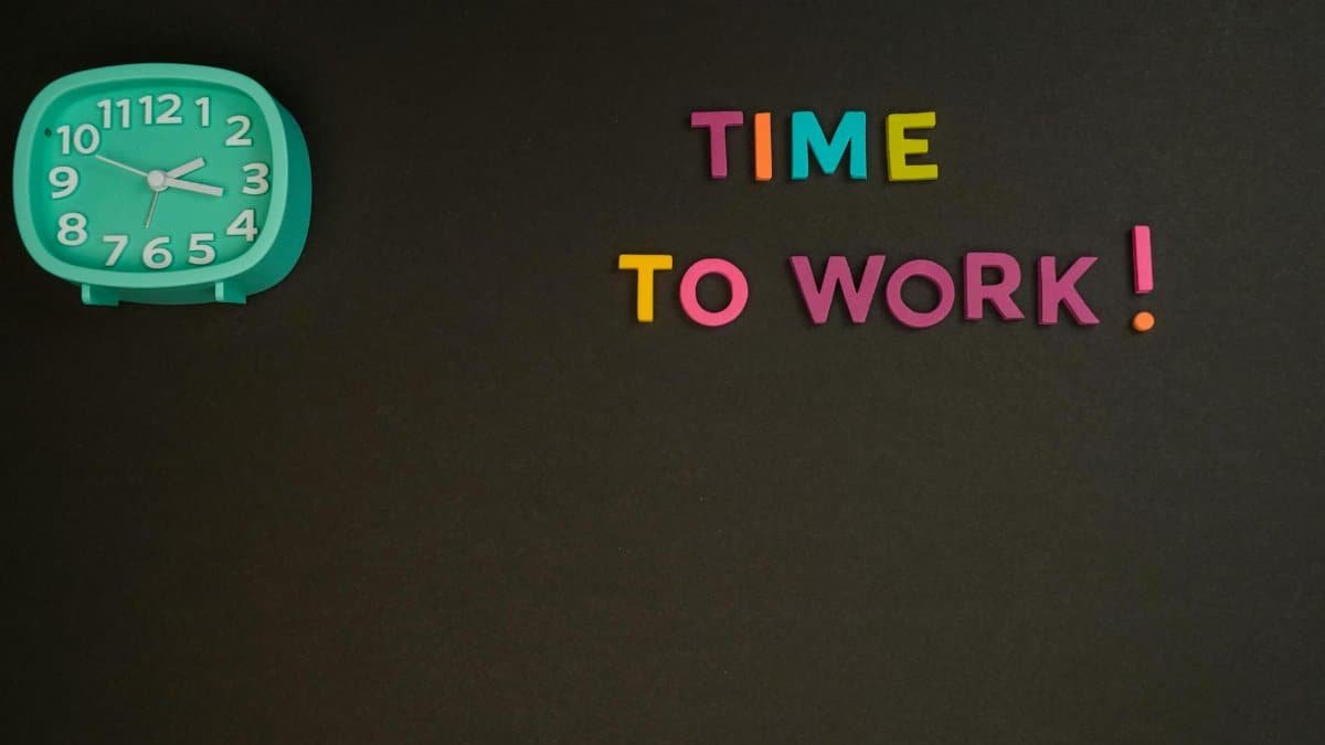 Minimalist image with a colorful clock and letters spelling 'Time to Work' on a black background.
