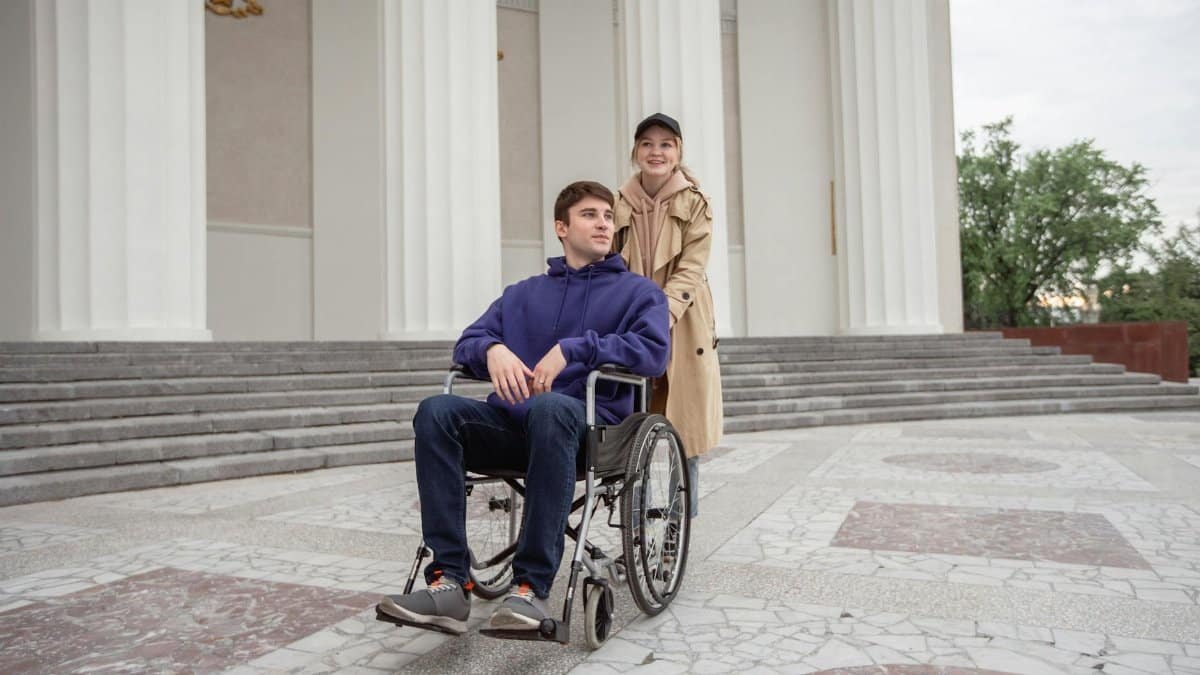 Woman assisting a man in a wheelchair outside a building with classical columns.