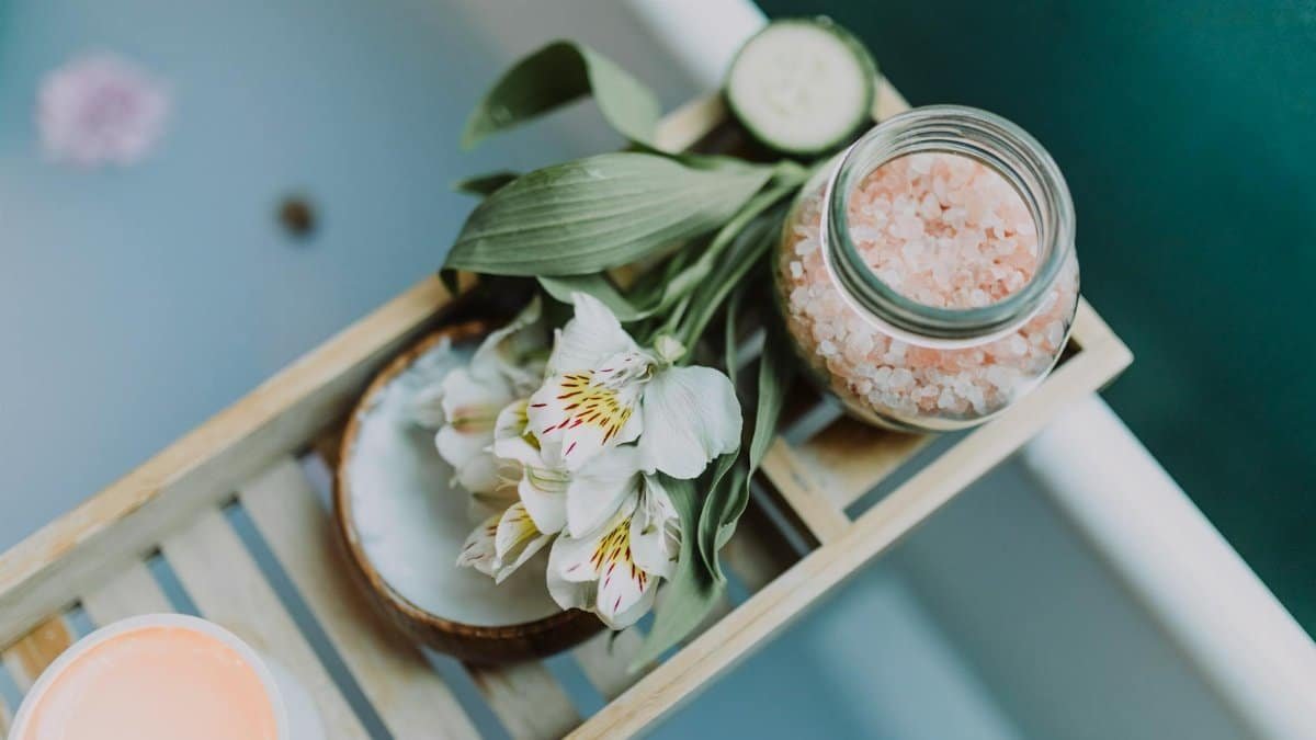 Spa essentials on a tray with Himalayan salt, flowers, and candles for a relaxing bath.
