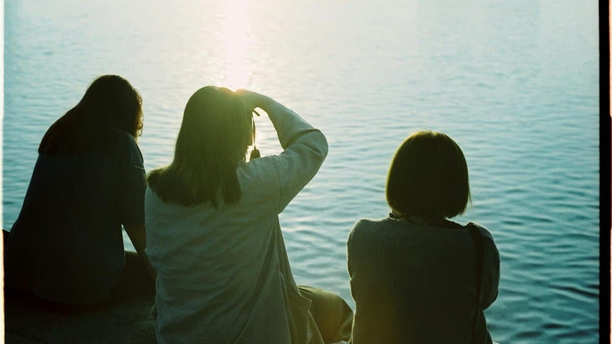 Silhouetted women sit by the water at sunset, capturing the serene moment of reflection.