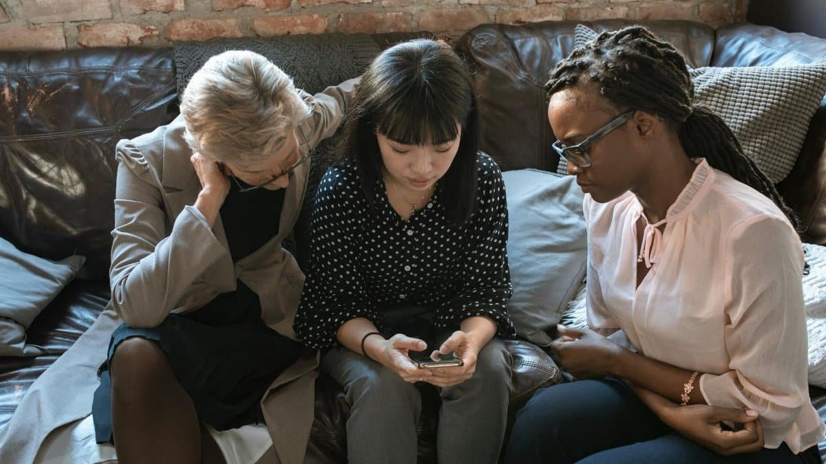 Three diverse women collaborating in a cozy office, fostering teamwork and creativity around a mobile device.