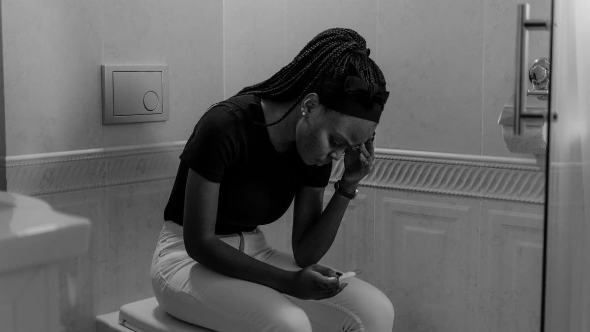 Black and white image of a young woman holding a pregnancy test, displaying anxiety.