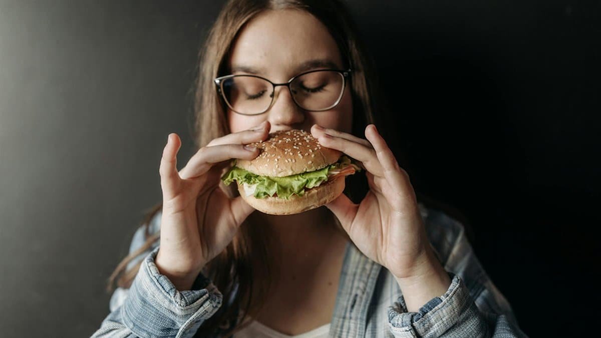 Young woman savoring a fresh burger indoors, depicting enjoyment of fast food.