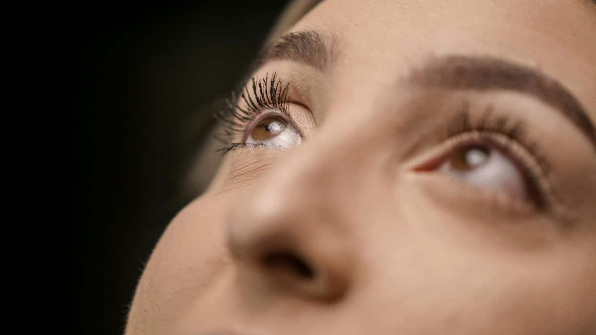A striking close-up photo of a woman's eyes gazing upward, emphasizing eyelashes and vision.