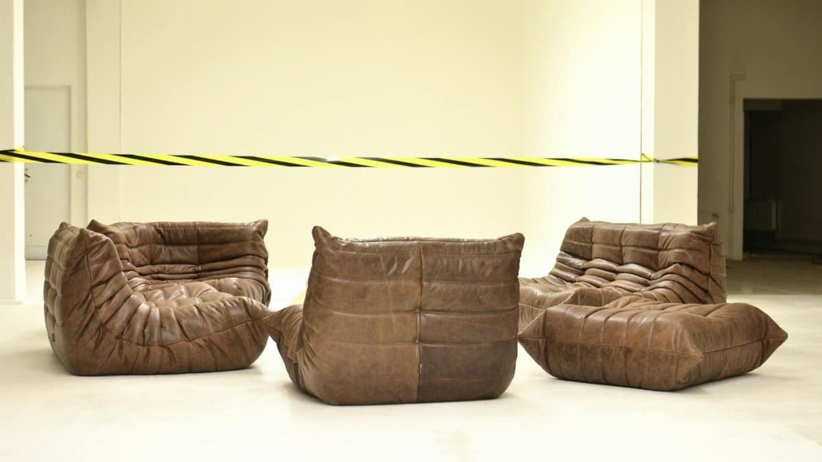 Leather couches placed in empty room under bright striped barrier tape during renovation process