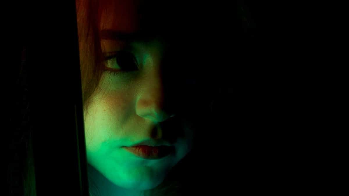 Artistic portrait of a woman with dramatic green and red lighting on a black background.
