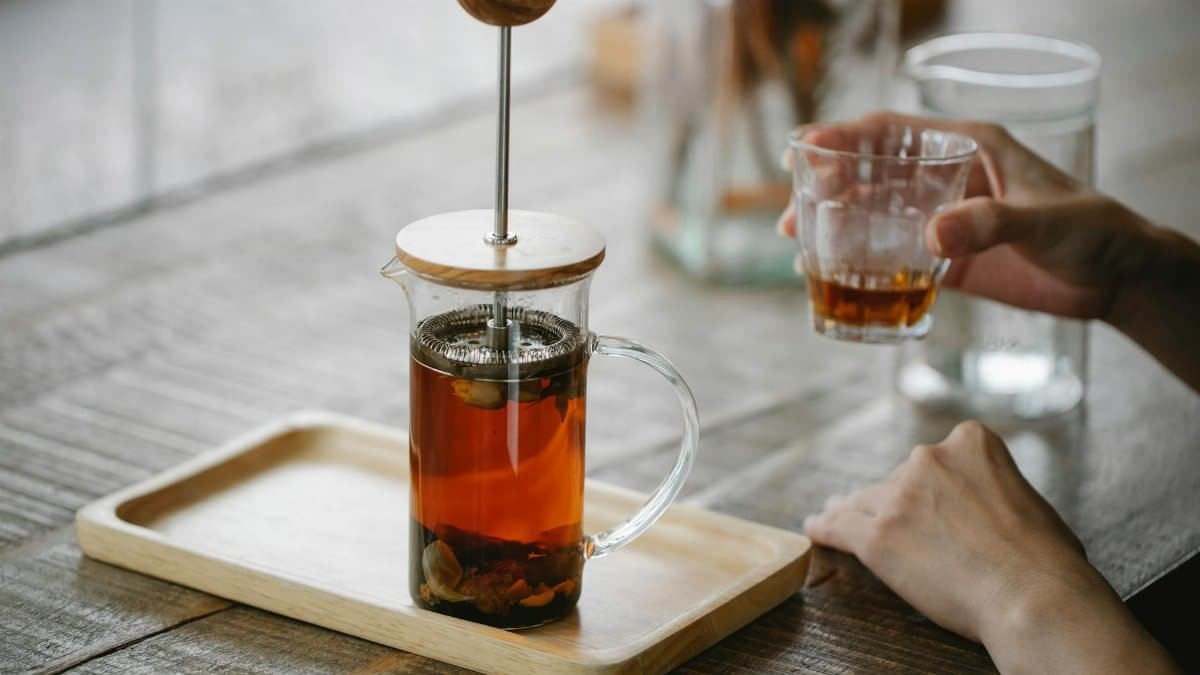 Glass teapot with tea and hand holding cup on wooden table, perfect for a calming tea break.