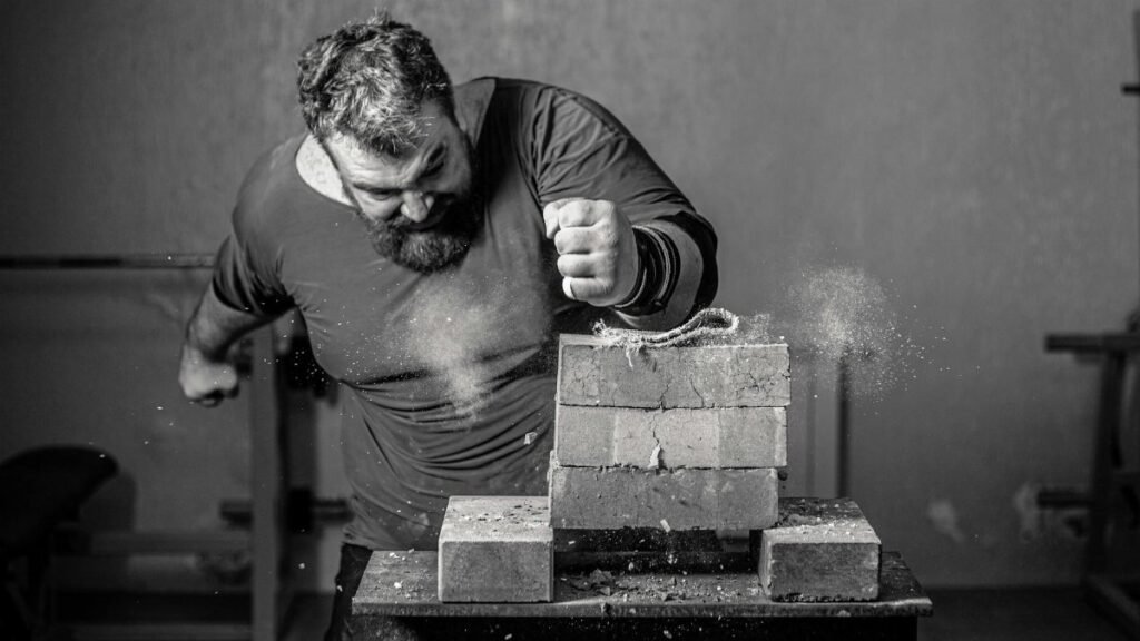 Dramatic grayscale image of a man breaking bricks indoors with powerful force.