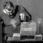 Dramatic grayscale image of a man breaking bricks indoors with powerful force.