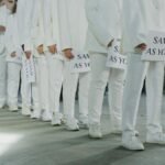 A group of individuals in white suits holding 'Same as You' signs, symbolizing unity and conformity.