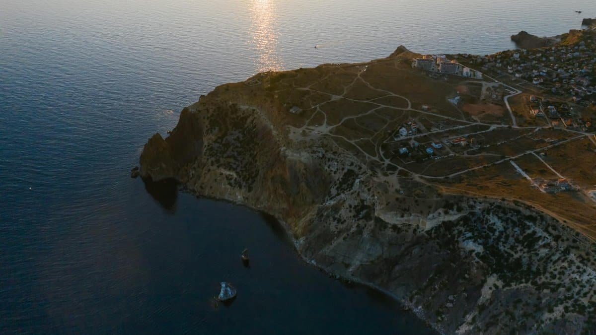 A breathtaking aerial shot of a coastal cliff and calm sea at sunset, showcasing natural beauty.