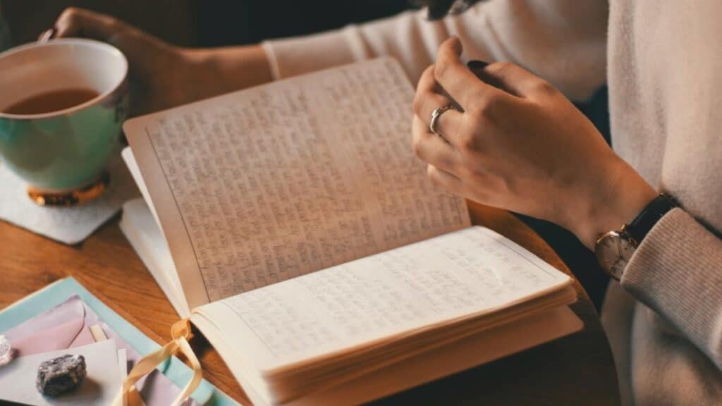 A woman writes in a journal while enjoying a cup of coffee at a wooden table.