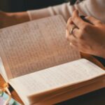 A woman writes in a journal while enjoying a cup of coffee at a wooden table.